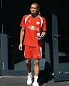 Fußballspieler im roten Trainingsoutfit steht im Türrahmen und hält einen Becher.
