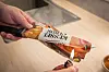 Hand verschließt eine gefaltete Chipstüte mit einem Feuerzeug auf der Kante.