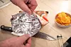 Hände verschließen eine Chiptüte mit Alufolie, daneben liegen Messer, Glas und Chipsschale.