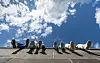 Vier Jugendliche sitzen auf einer Mauer am Hafenpark und baumeln mit den Beinen vor wolkigem Himmel.