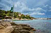 Playa de Illetes auf Mallorca mit Felsen, türkisblauem Wasser und Hügelhäusern unter Wolken.