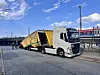 Schwerlast-Lkw zieht gelben Güterwagen neben einer Bahnstrecke.