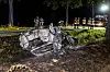 Ausgebranntes Auto liegt auf der Seite im Straßengraben, Feuerwehrleute und Rettungskräfte sichern die Unfallstelle.