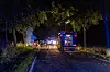 Feuerwehrfahrzeuge und Einsatzkräfte auf einer dunklen Landstraße bei Blaulicht und Rauch.