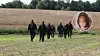 Mehrere Polizisten gehen über ein Feld, rechts ein eingeblendetes Porträt.