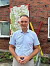 Mann steht vor Stadtplan an Backsteinwand mit farbigen Metallstangen.