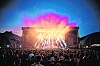 Große Menschenmenge vor heller Konzertbühne mit buntem Licht und Rauch bei Open-air-Veranstaltung.