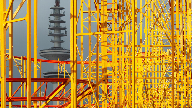Strommast zwischen gelben Stahlgerüsten in einem Umspannwerk.