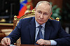 Putin sitzt im Kreml am Tisch, hört dem Wissenschaftsminister zu, russische Flaggen im Hintergrund.