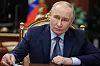 Putin sitzt im Kreml am Tisch, hört dem Wissenschaftsminister zu, russische Flaggen im Hintergrund.