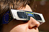 Person trägt eine Lichtschutzbrille mit EU-Motiv für die Beobachtung der partiellen Sonnenfinsternis.