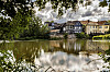 Fachwerkhäuser in Marburg spiegeln sich in der Lahn unter wolkigem Himmel, umrahmt von Bäumen.