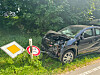Schwarzes Auto mit Frontschaden neben umgestürztem Verkehrsschild am Straßenrand.