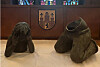 Zweiteilige Bronze „Trauerndes Kind“ liegt auf einem Tisch, dahinter ein Wappen an der Wand.