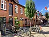 Fahrräder vor roten Backsteinhäusern, darüber bunte Wimpel und ein Baum an sonniger Straße.
