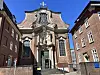 Barocke Kirche mit Kreuz, Treppe und Eingang zwischen Backsteingebäuden.