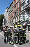 Feuerwehrleute stehen auf einer abgesperrten Straße vor Gebäuden und Geschäften.