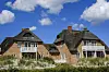 Reetgedeckte Backsteinhäuser mit Balkonen stehen in St. Peter-Ording vor blauem Himmel.