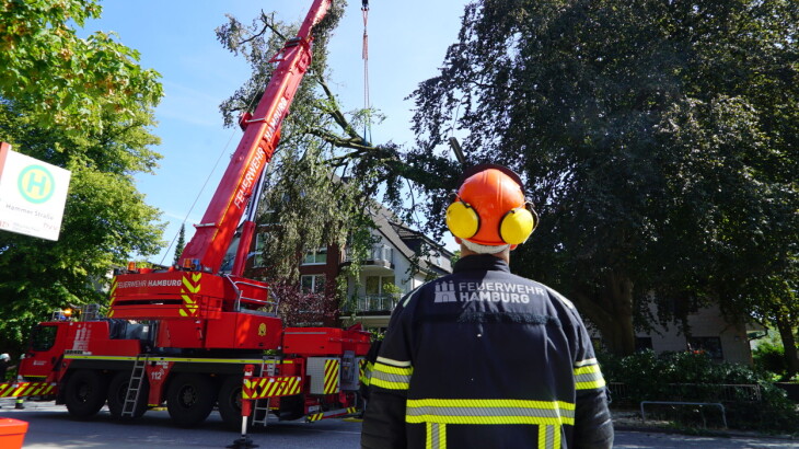 Feuerwehrmann mit Helm steht neben rotem Einsatzfahrzeug mit ausgefahrener Drehleiter.