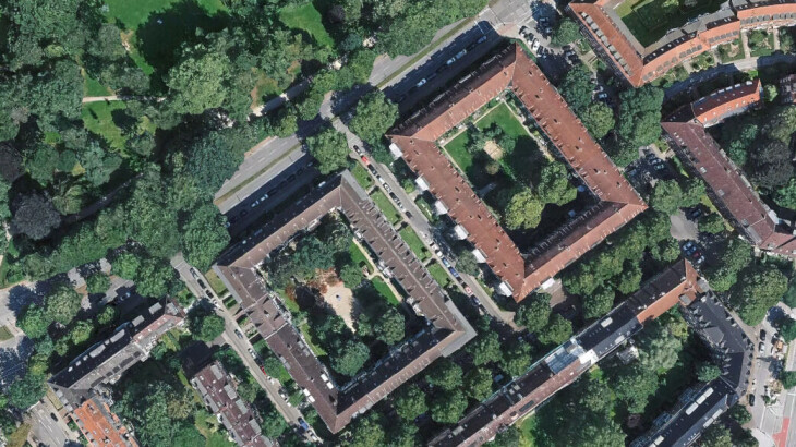 Luftaufnahme eines begrünten Gebäudekomplexes mit Innenhöfen, Bäumen und umliegenden Straßen