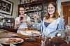 Leni (l) und Minna filmen im Cafe Deike hinter der Theke mit Kuchen und Getränken ihre Videos für Instagram.