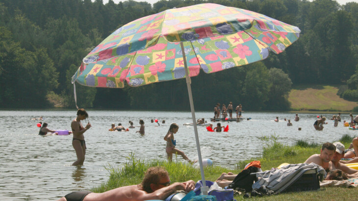 Badegäste schwimmen und sonnen sich am Twistesee bei Wetterburg unter einem bunten Sonnenschirm.