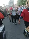Trommelgruppe marschiert durch eine belebte Fußgängerzone, umgeben von Zuschauenden.