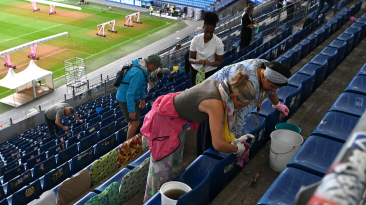 Freiwillige reinigen Sitzplätze im Volksparkstadion mit Eimern und Tüchern.