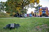 Mehrere Einsatzfahrzeuge stehen an einer Landstraße, ein Feuerwehrfahrzeug rechts, dunkler Gegenstand im Gras vorn.