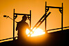 Bauarbeiter als Silhouette zwischen Stahlträgern vor leuchtendem Sonnenuntergang auf einer Baustelle