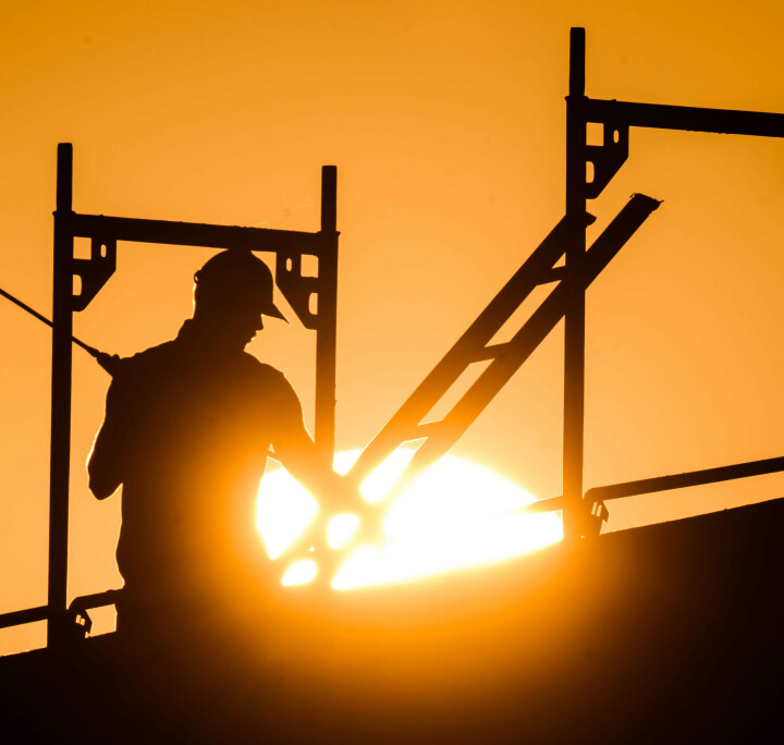 Bauarbeiter als Silhouette zwischen Stahlträgern vor leuchtendem Sonnenuntergang auf einer Baustelle
