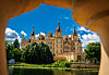 Schweriner Schloss am Burgsee, eingerahmt von einem Steingeländer, bei blauem Himmel und Sonnenschein.