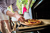 Familie bereitet auf einer Terrasse gemeinsam eine Pizza am Grill zu.