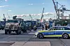 Polizeiwagen steht vor Kränen und Lastwagen in einem Industriehafen.