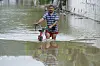 Mann schiebt ein Fahrrad durch knietiefes Hochwasser in Santa Ana, Ecuador.