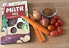 Packung „Matr Hack“ neben Karotten, Zwiebeln, Tomaten und einer Schale mit braunem Granulat