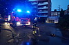 Feuerwehrfahrzeug mit Blaulicht und Einsatzkraft auf nasser Straße bei Nacht