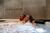 Zwei Personen entspannen im sprudelnden Whirlpool unter dem Schriftzug „MYWELLNESS“.