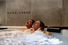 Zwei Personen entspannen im sprudelnden Whirlpool unter dem Schriftzug „MYWELLNESS“.