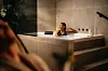 Frau entspannt in einer luxuriösen Badewanne mit Natursteinwänden und gedämpfter Beleuchtung.