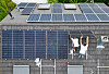 Zwei Arbeiter installieren Solarmodule auf dem Dach eines Privathauses.