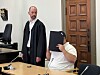 Mann in schwarzer Robe steht neben einem Tisch, daneben sitzt ein Mann mit schwarzer Mappe.