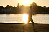 Jogger läuft bei Sonnenaufgang am Ufer der Alster, im Hintergrund Wasser, Bäume und Häuser.