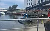 Kleines Boot im Hafenbecken vor einer belebten Uferpromenade mit Menschen und Gebäuden