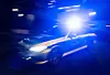 Polizeifahrzeug mit blauem Blinklicht fährt nachts an einem Gebäude vorbei.