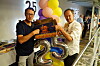 Zwei Männer halten eine Schokoladentorte und silberne Ballons mit der Zahl 25.