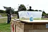 Zwei Personen arbeiten an einer mobilen Station mit transparentem Behälter auf einer Wiese.