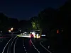Fahrzeuge fahren nachts über eine kurvenreiche, von Bäumen gesäumte Straße.