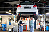 Zwei Mechaniker arbeiten unter einem angehobenen Mitsubishi-SUV in einer Kfz-Werkstatt.