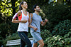 Eine Joggerin und ein Jogger laufen gemeinsam durch einen grünen Park.